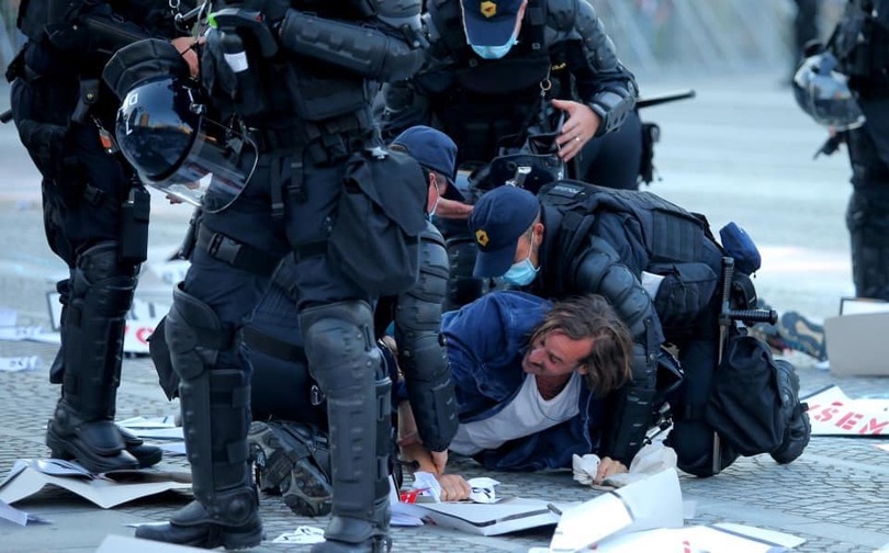 Slika 37 (spodaj). Joško Suhadolnik, brez naslova (umetnik Jaša Mrevlje Pollak, ki ga policisti pritiskajo ob tla, ker je preskočil ograjo, ki jo je vlada postavila na Trgu republike, da bi preprečila proteste), 12. junij 2020.